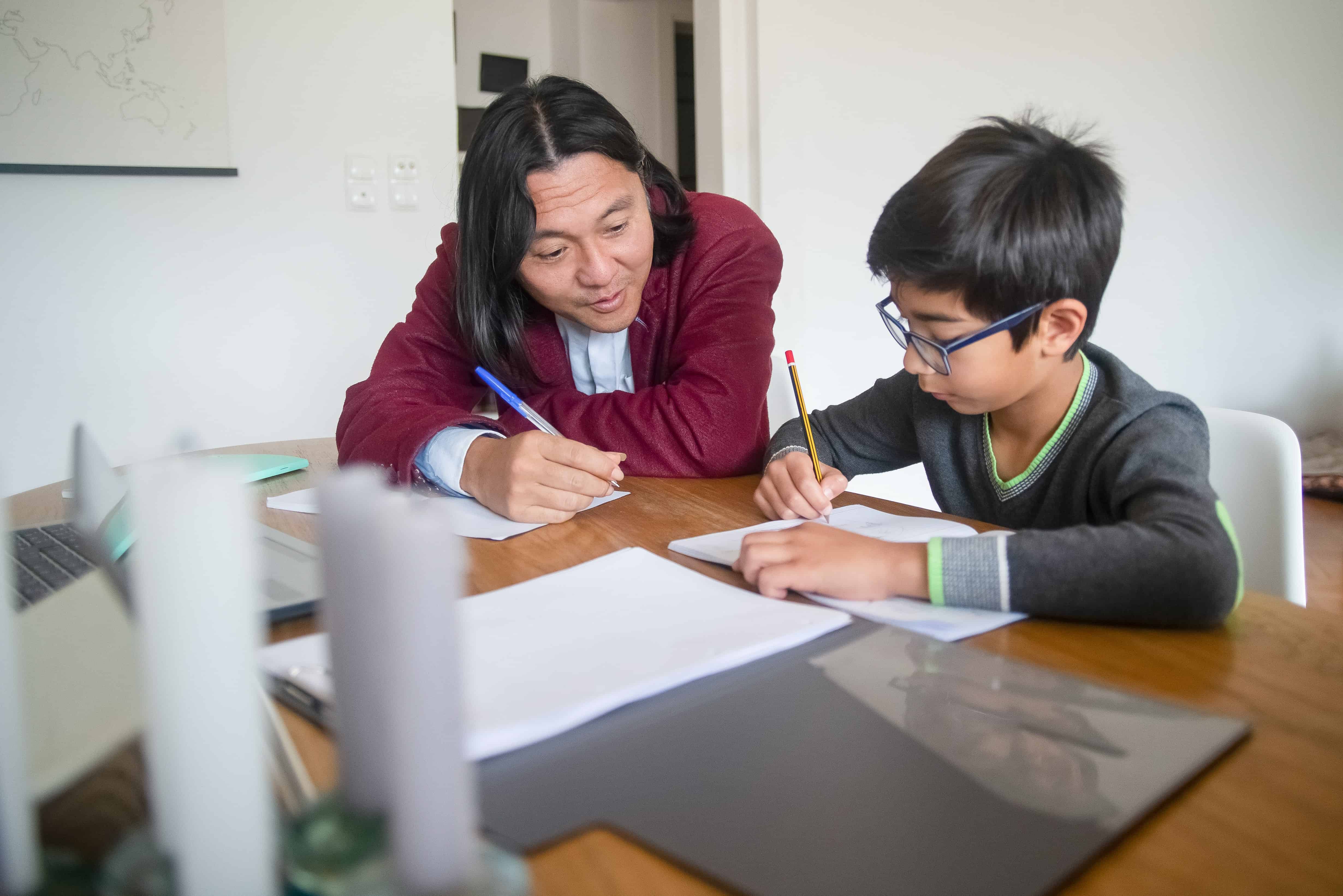 father helping child with homework on desk