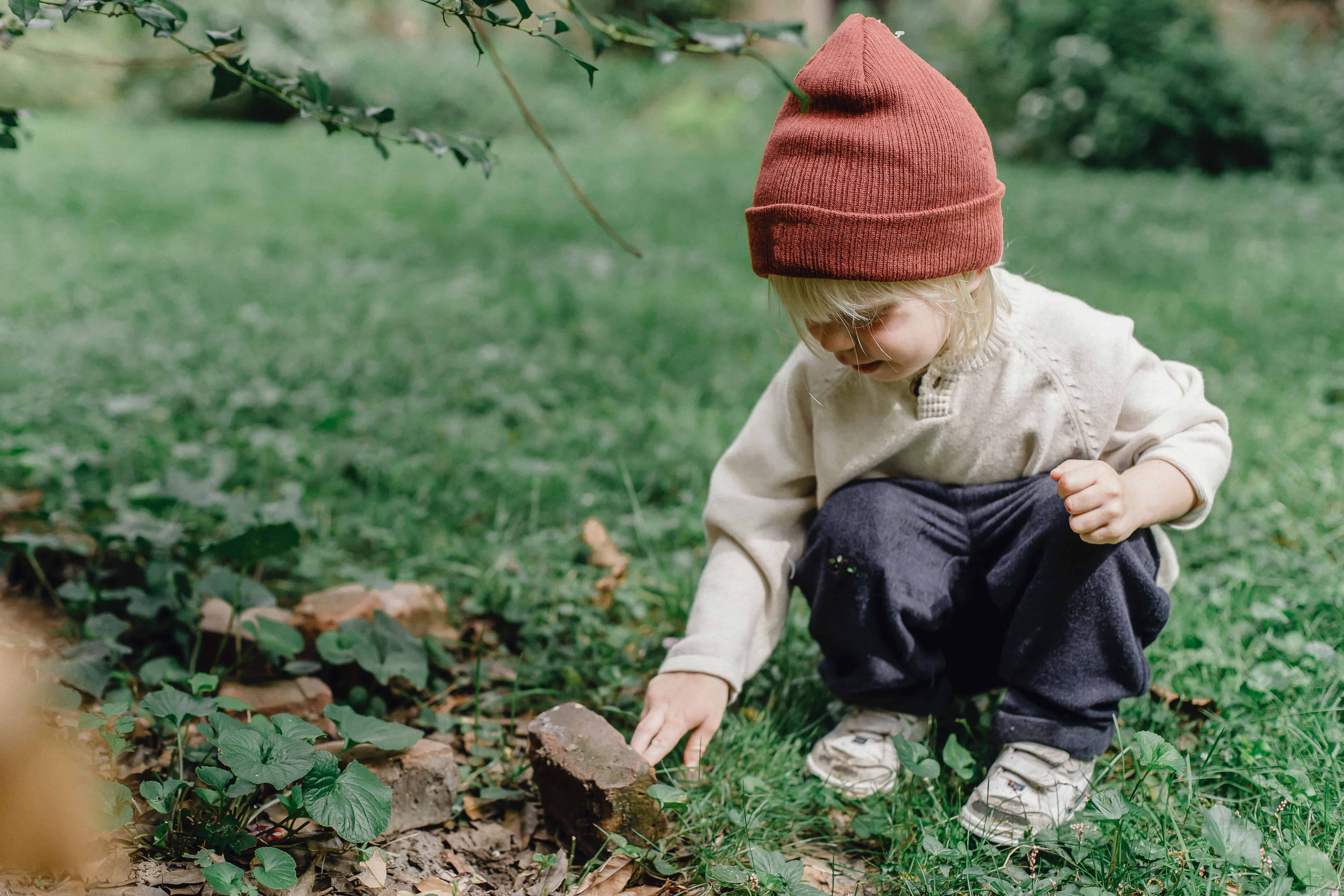 child in beanie crouching in the grass