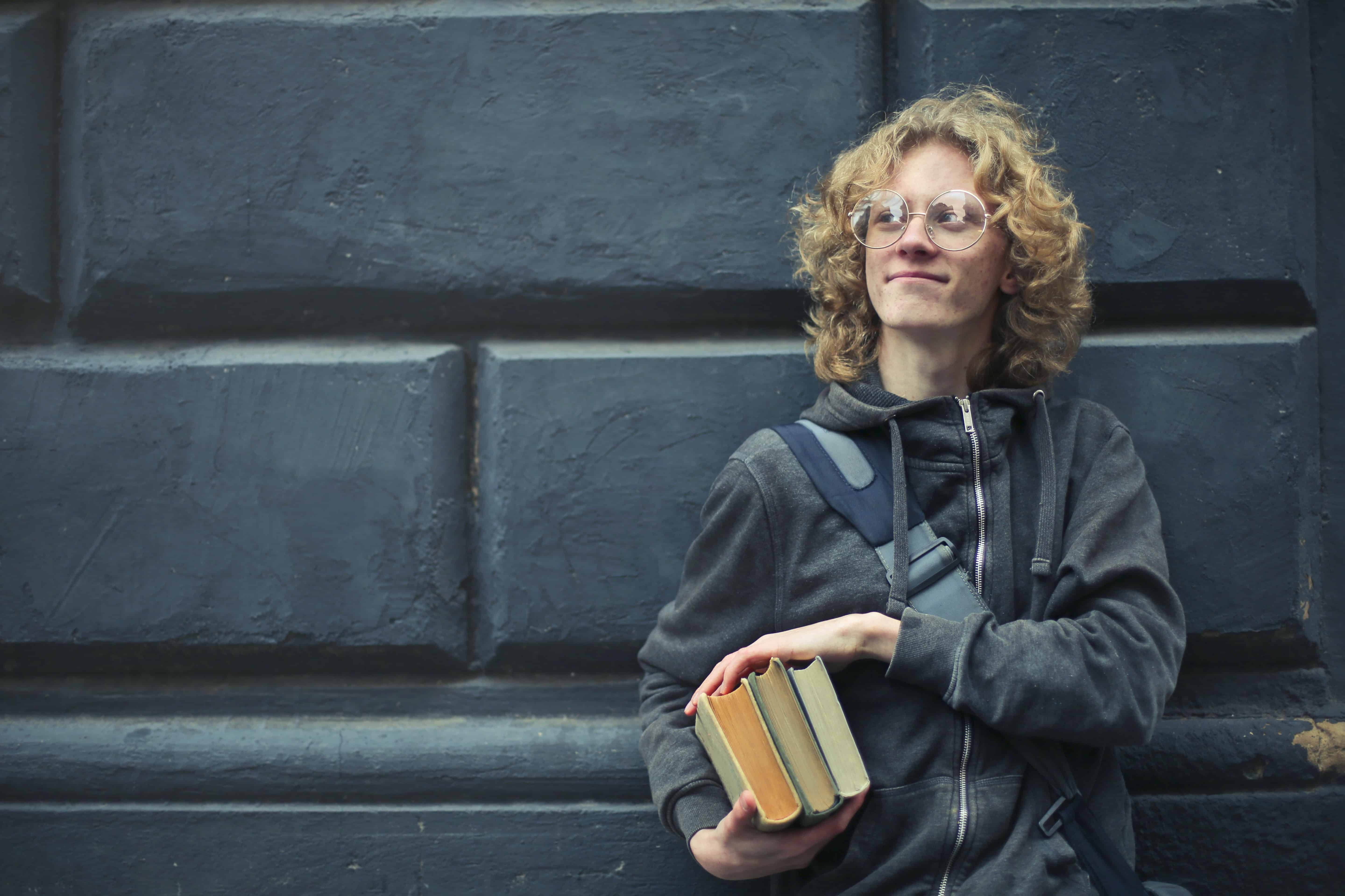 kid with books and backpack in front of dark brick wall