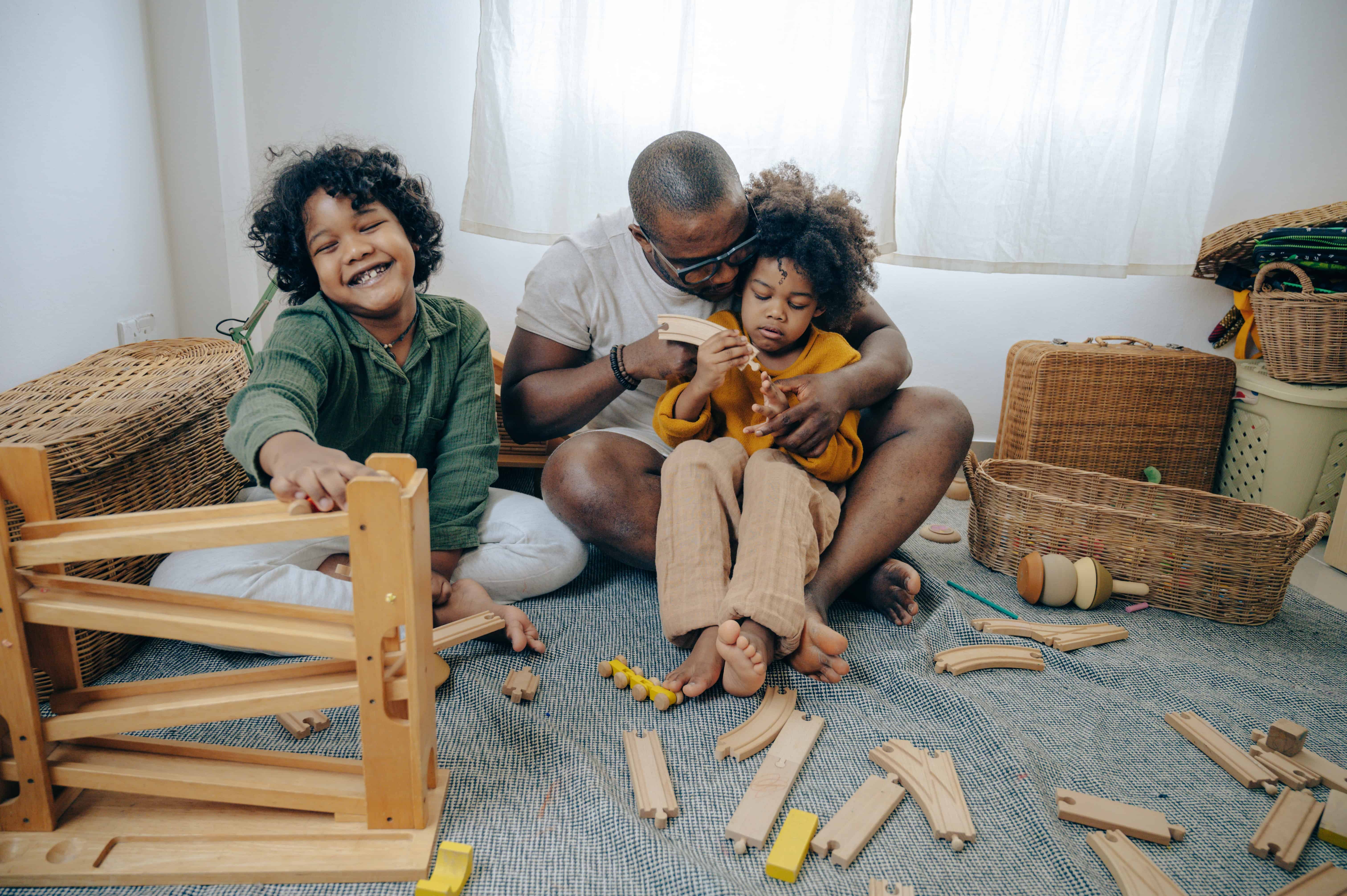 father playing with wooden trains with two children